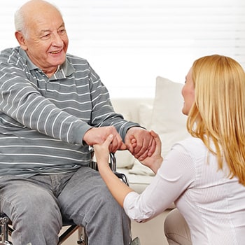 Pflegekraft von Iwona Szwedyc hält die Hände eines Rentners der im Rollstuhl sitzt